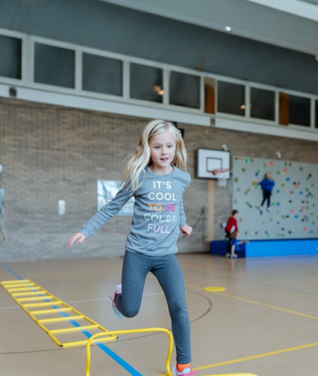 Primary School student jumping in an indoor gym during a sports activity.