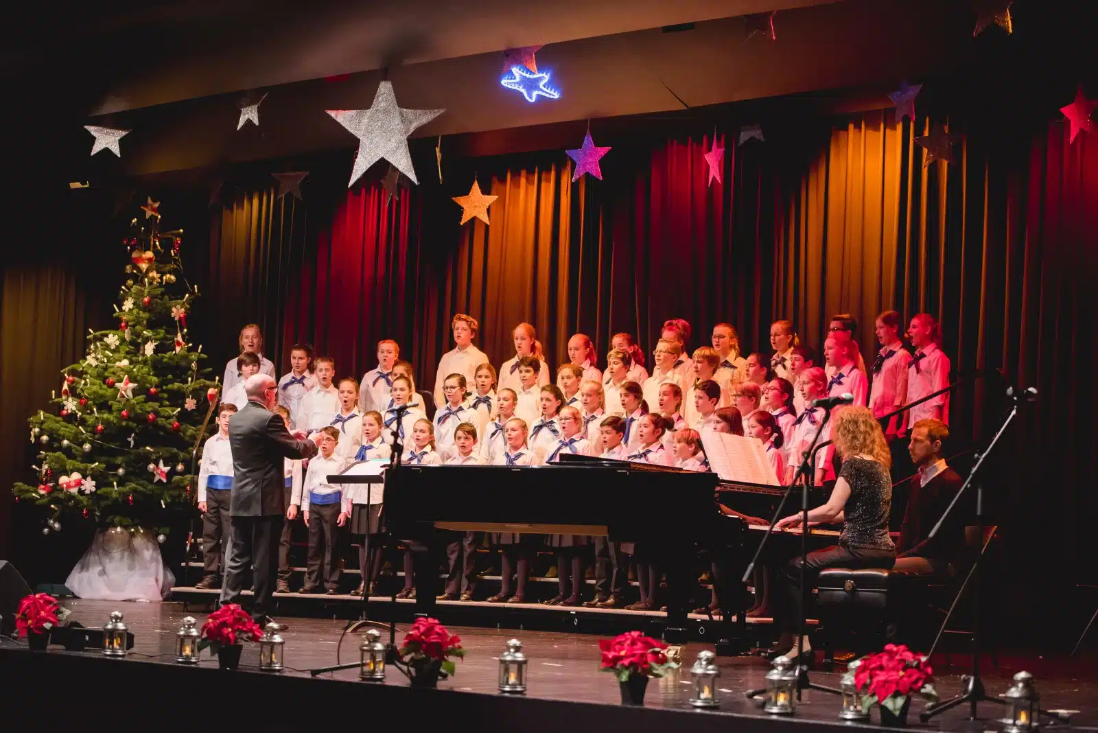 Children singing in the school choir with the director conducting and a pianist accompanying them.
