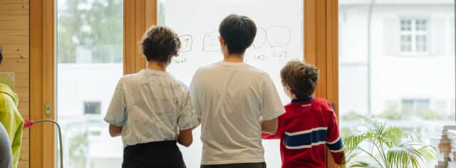 Three students seen from behind, looking out of a window.