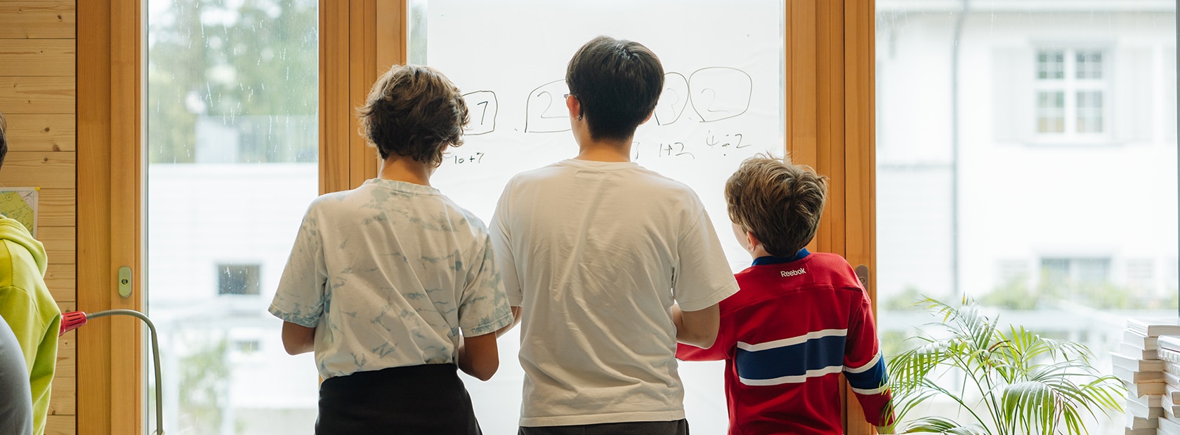 Three students seen from behind, looking out of a window.