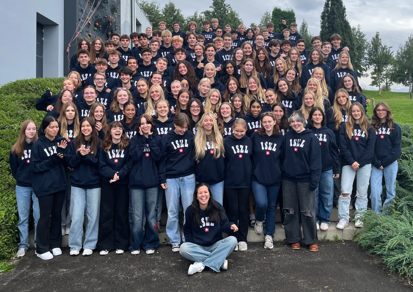class 2025 High School students gathered together outside the school building, smiling and enjoying the campus environment.