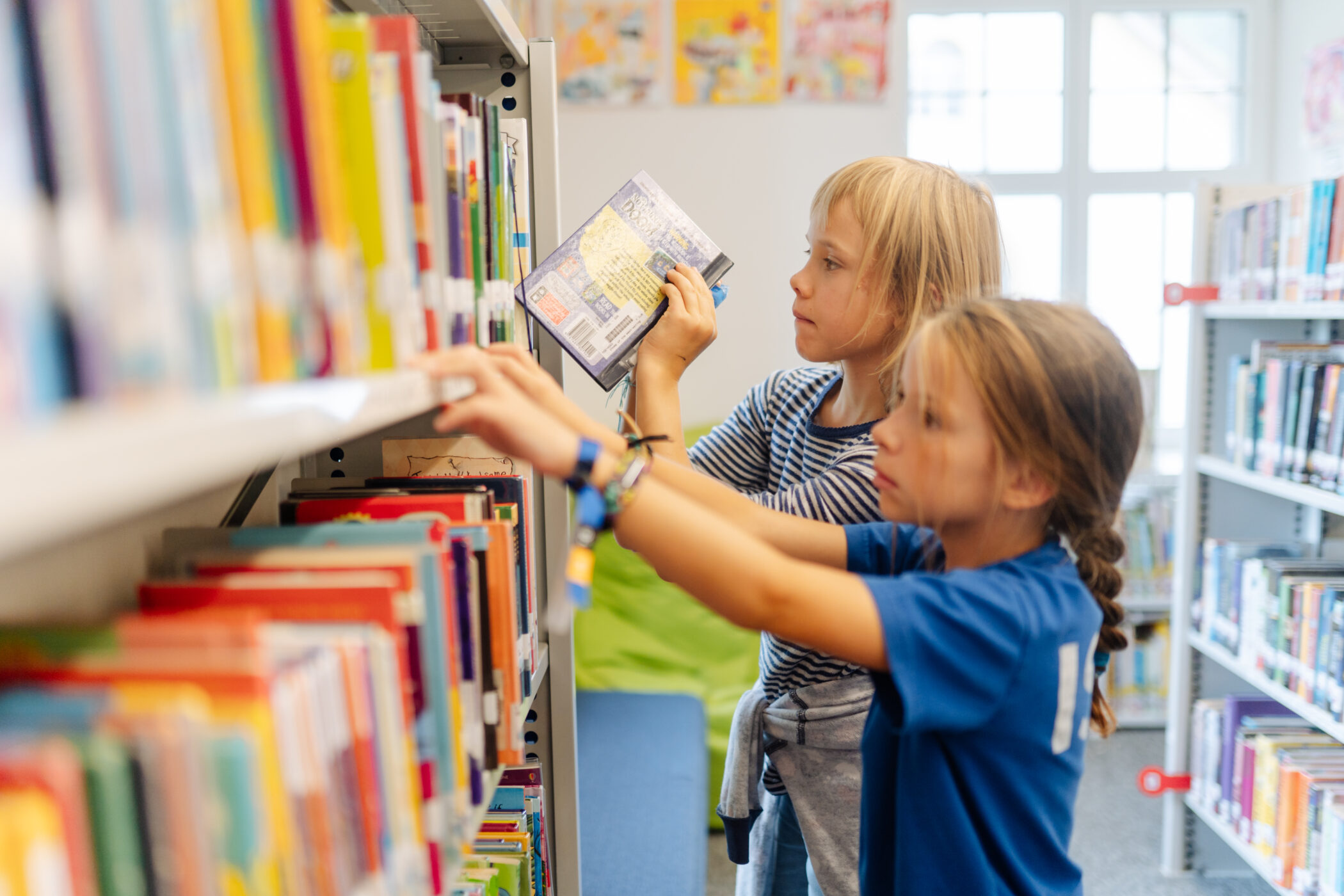 Two primary school girls selecting books from a shelf in the ISZL school library.