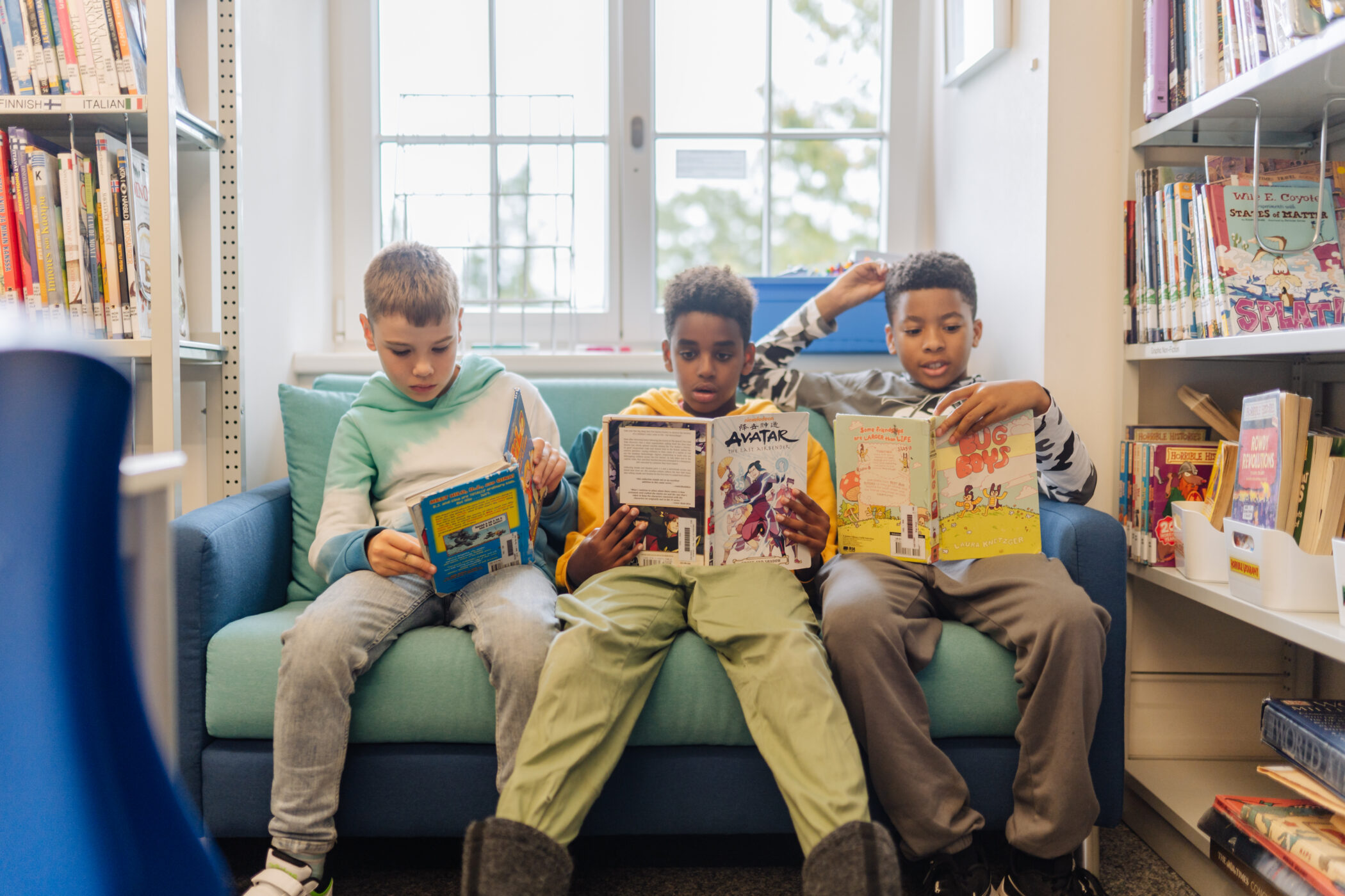 Three students reading books while sitting on a sofa in the library at the Zug campus.