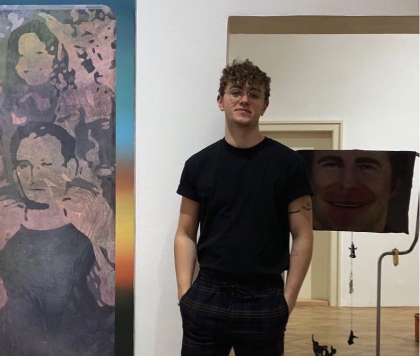 **Alt Text:** ISZL alumnus Luke McCowan standing beside his artwork.