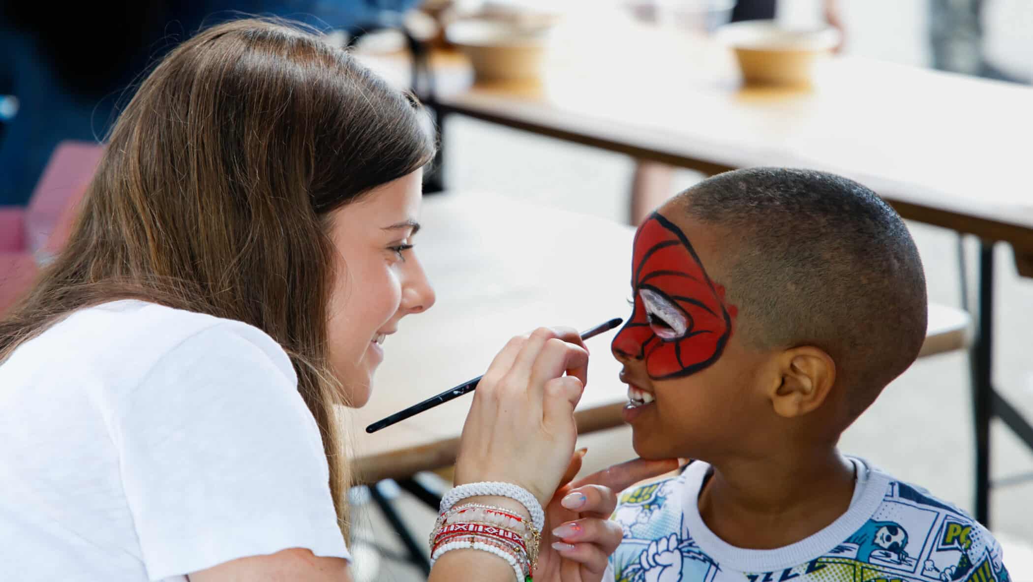 A student painting a child’s face in a Spider-Man design during a face-painting activity.