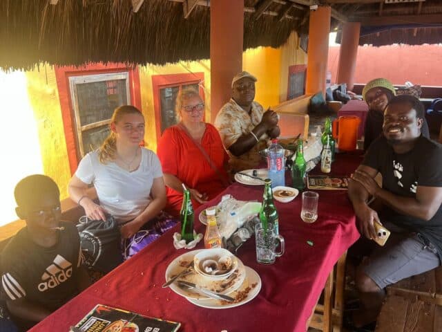 Six adults and one child sitting around a table at an open-air restaurant, with plates and drinks visible after a shared meal.