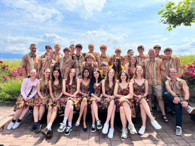 Group of students and adults posing outdoors in matching patterned clothing, seated and standing together in a garden setting.