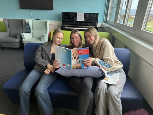 Three students sit together reviewing first aid course materials in preparation for their certification assessment.