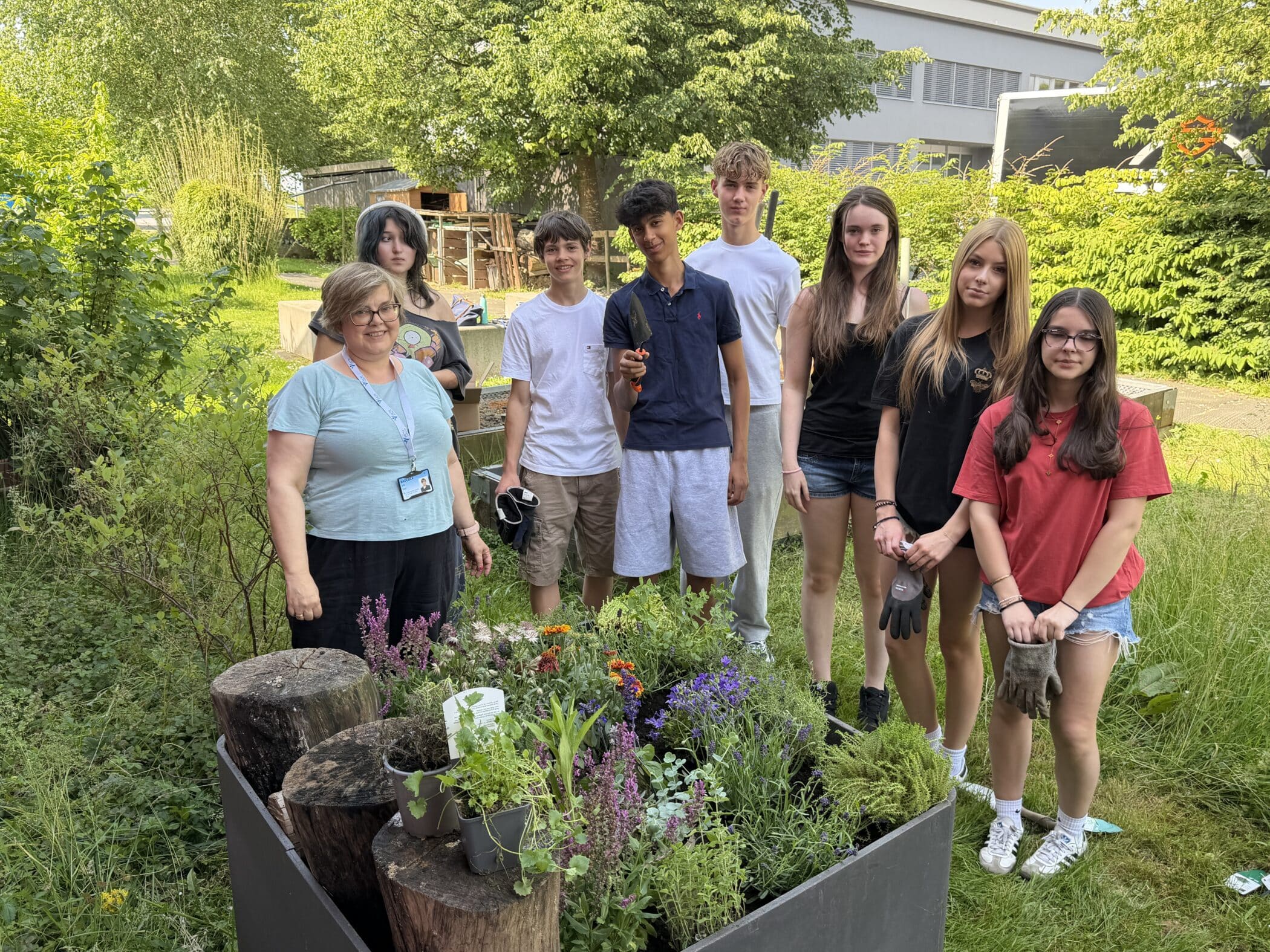 Students and staff gather around a newly planted biodiversity-friendly planter filled with pollinator-friendly flowers and herbs in the school garden.