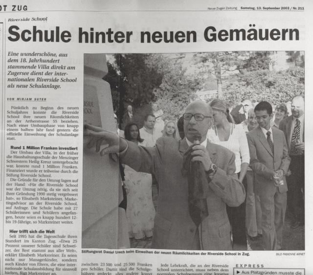 Black-and-white newspaper article from 2003 featuring Daniel Urech speaking at the opening of the Riverside School’s new campus in Zug, surrounded by students, staff, and guests.